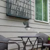 An outdoor patio scene with a wall-mounted light fixture and outdoor furniture. Produktbild-Vorschau