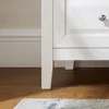 A close-up view of the bottom corner of a white cabinet with a drawer knob, resting on a wooden floor. Náhľad obrázku produktu