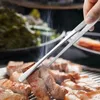 A hand is using kitchen tongs to turn pieces of meat cooking on a grill. Steam is rising from the meat. Produktbild-Vorschau