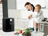 A woman is holding a baby in a kitchen, with an air fryer and salad ingredients on the counter. Anteprima dell’immagine prodotto