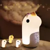 A large unicorn night light with a digital clock display and three smaller unicorn figures in the foreground, set against a dark, smoky background with hanging gold stars and moons. Produktbild-Vorschau