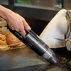 A hand is holding a black handheld vacuum cleaner and cleaning crumbs off a countertop next to a food slicer and a tray of bread. Podgląd zdjęcia produktu