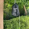 A black camping shower bag is hanging from a tree branch, with a green hose extending downwards. Produktbild-Vorschau