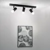 A black ceiling light fixture with three adjustable spotlights is mounted on a white ceiling above a framed piece of art with a circular pattern. Náhľad obrázku produktu