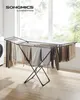 A SONGMICS clothes drying rack is shown in a laundry room setting, with clothes hanging on it, next to a washing machine and in front of a large window. Produktbild-Vorschau