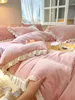 A hand is shown touching a pink plush bedding set with ruffles, with a window and curtains in the background. Produktbild-Vorschau