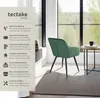 A green velvet chair is shown next to a small round table with a black mug on it, in a room with large windows overlooking a forest. A text overlay on the left describes the chair's features. Produktbild-Vorschau