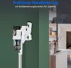 A white cordless vacuum cleaner is mounted on a wall bracket against a green wall, with a living room scene visible on the right. Produktbild-Vorschau