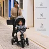A woman is pushing a young child on a tricycle on a cobblestone street. Produktbild-Vorschau