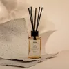 A reed diffuser with red cedar scent is placed on a textured surface with soft lighting and shadows. Podgląd zdjęcia produktu