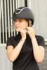 A woman is adjusting her riding helmet outdoors. Produktbild-Vorschau