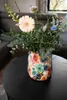 A colorful floral vase filled with flowers sits on a black coffee table. Voir les images du produit