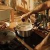 A person is cooking on a stovetop, lifting the lid off a pot. Podgląd zdjęcia produktu