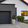 A modern house with a garage and a window, featuring potted plants on the driveway. Produktbild-Vorschau