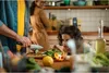 A family is preparing food in a kitchen. A man is chopping vegetables, a child is watching, and a woman is in the background. Podgląd zdjęcia produktu