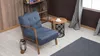 A blue armchair with wooden frame in a living room setting, next to a side table and a rug. Produktbild-Vorschau