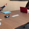Two people are in a meeting room, one is speaking and gesturing, the other is looking at a laptop. Produktbild-Vorschau
