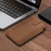 A brown leather phone case is placed on a wooden surface next to a laptop and a black wallet. Produktbild-Vorschau