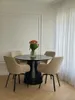 A dining set with a round table and four chairs in a room with white walls and sheer curtains. Produktbild-Vorschau