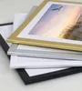 A stack of four picture frames in different colors (gold, silver, white, and black) on a white and light gray background. Produktbild-Vorschau