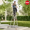 A man is using a ladder to trim tree branches in a garden. Produktbild-Vorschau