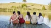 A group of friends sitting on a wooden dock by a lake, with a portable speaker on the dock. Produktbild-Vorschau