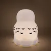 A white owl-shaped lamp with black feather markings, illuminated from within, against a brown background. Anteprima dell’immagine prodotto