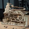 A wooden marble run model with gears and tracks, set on a surface covered in wood shavings. Náhľad obrázku produktu
