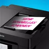 A close-up shot of a black Epson printer with a piece of paper showing pink text being fed into the scanner. Náhľad obrázku produktu