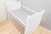 A white baby crib with a gray and white polka dot fitted sheet. Produktbild-Vorschau