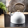 A white kettle with wood accents sits on a black induction stovetop. Podgląd zdjęcia produktu