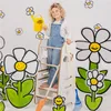 A young child stands on a wooden learning tower, holding a yellow watering can, surrounded by large cartoon flowers. Náhled obrázku produktu
