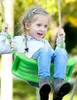 A young girl is happily swinging on a green swing set outdoors. Náhľad obrázku produktu