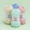 Four balls of yarn with sequins are arranged diagonally on a light green background. Produktbild-Vorschau