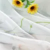 A close-up view of a white sheer curtain with green embroidered floral patterns and two yellow sunflowers. Produktbild-Vorschau