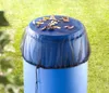 A blue rain barrel covered with a black mesh net, with leaves on top, in a grassy outdoor setting. Náhľad obrázku produktu