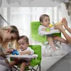 Zwei Babys in grünen tragbaren Hochstühlen, eines spielt mit einem blauen Spielzeugauto, das andere wird gefüttert Náhled obrázku produktu