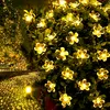 A string of solar-powered flower-shaped lights illuminating a garden path and bushes at night. Produktbild-Vorschau