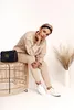 A woman is sitting on a wicker stool next to a black Gucci handbag, posing for a photo. A tall vase with dried grass is in the background. Podgląd zdjęcia produktu