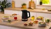 A black electric kettle is placed on a kitchen counter surrounded by various bowls of food and cups of tea. Anteprima dell’immagine prodotto