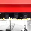 Close-up of the control panel of a red popcorn machine, showing three switches labeled 'TURN', 'HEAT', and 'WARM LIGHT'. Popcorn kernels are visible at the bottom. Voir les images du produit