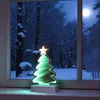 A decorative LED Christmas tree with an infinity effect sits on a windowsill overlooking a snowy forest scene at night. Produktbild-Vorschau