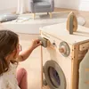 A young girl is playing with a wooden toy washing machine in a room. Produktbild-Vorschau