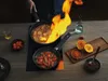 A person is cooking with two pans on a stovetop, one of which is flaming. Podgląd zdjęcia produktu