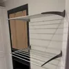Two wall-mounted drying racks are shown on a light gray wall next to a dark-framed window with a tan curtain. Produktbild-Vorschau
