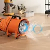 An industrial fan with a flexible hose is shown in a room with other equipment in the background. Produktbild-Vorschau