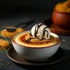 A close-up of a dessert in a bowl, topped with ice cream and chocolate sauce. Produktbild-Vorschau