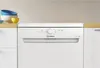 A white Indesit dishwasher is shown in a kitchen setting, with some bowls on the counter to the left. Voir les images du produit