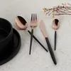 A set of cutlery with rose gold heads and black handles is arranged on a light-colored surface, with a black bowl and plate in the foreground. Náhľad obrázku produktu