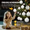 A young girl is decorating a Christmas tree with white ornaments. Anteprima dell’immagine prodotto